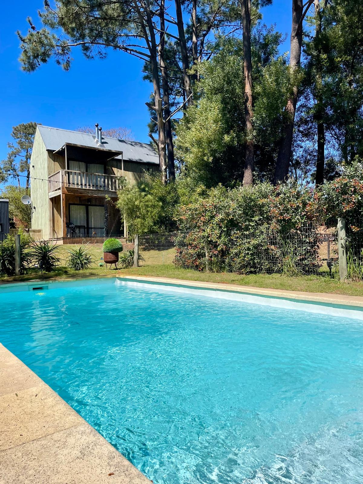 La pileta de Villa Mora con el bungalow y el bosque detrás